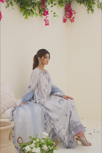 VIDEO: odel wearing a light grey formal embroidered suit, turning around to display the outfit's fit, fabric texture, and flow of the blue dupatta.
