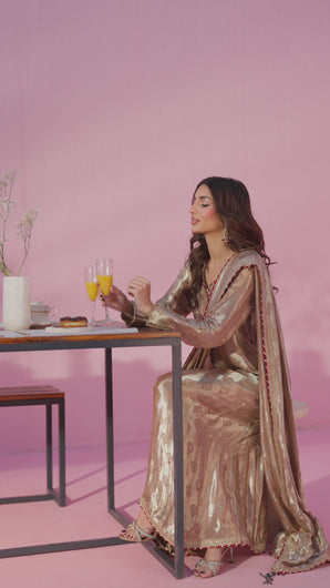 Video shows model in Maina ensemble, pure Mysori jamawar silk maxi in radiant gold with hand‑embellished neckline, emerald and deep red accents, and attached dupatta.
