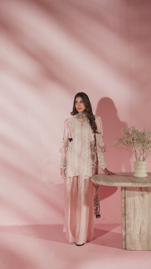 Video of model walking in Malina powder pink sheesha silk Eid set, captured from multiple angles with scalloped edges, lace panels, and handworked cuffs, styled with wide‑leg trousers and flowing khaddi net dupatta. 
